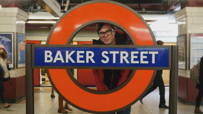 Ralph Caspers hinter einem Schild, auf dem "Baker Street" steht