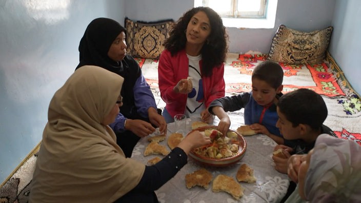 Siham sitzt mit einer Familie auf dem Boden, sie essen Tajine