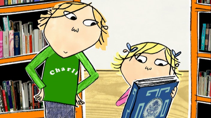 Charlie steht neben Lola, die ein blaues Buch in der Hand hält