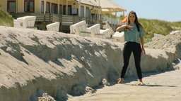 Clarissa steht am Strand und zeigt Höhe an
