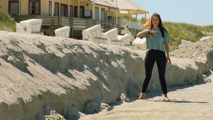 Clarissa steht am Strand und zeigt Höhe an