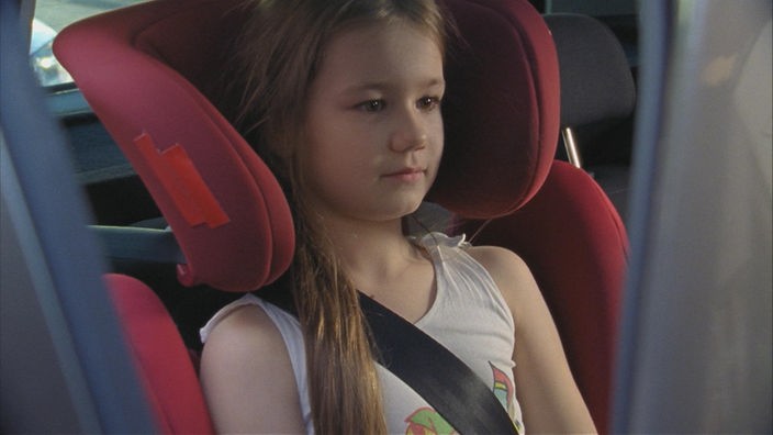Mädchen sitzt in einem roten Kindersitz im Auto