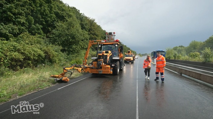 Ein Rasenmäher mäht den Grünstreifen an einer Autobahn.