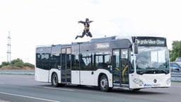 Ein an Seilen gesichterter Mensch springt auf einem fahrenden Bus.