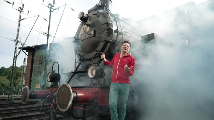 André steht vor einer dampfenden Lokomotive.