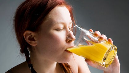 Ein Mädchen trinkt an einem Glas mit Orangensaft.