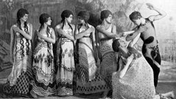 Gruppe bestehend aus sechs Tänzerinnen und einem Tänzer mit Perücken und bunten Kleidern.