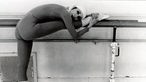 Schwarz-weiß Aufnahme der brasilianischen Tänzerin Macria Haydée an einer Ballettstange über ein Bein gebeugt stehend
