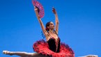 Aufnahme aus der Aufführung „Don Quichote“, bei der die Solotänzerin Polina Semionova in der Luft während eines Spagatsprungs in einem klassischen, rot-schwarzen Tutu mit Fächer in der Hand zu sehen ist. 
