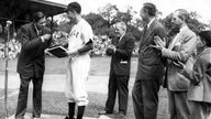 Schwarz-weiß-Foto: Spieler 'Babe' Ruth überreicht einem Offiziellen ein Buch auf dem Spielfeld.