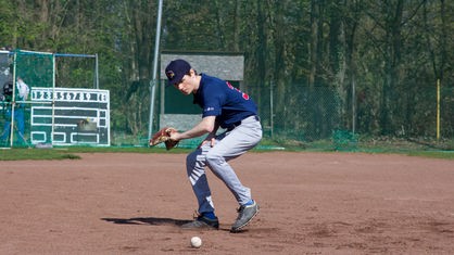 Johannes beim Baseball-Training mit Handschuh, Ball liegt vor ihm auf dem Boden.