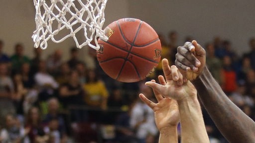 Hände mit Ball strecken sich Richtung Basketballkorb.