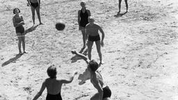 Schwarz-weiß Foto: Menschen spielen Volleyball an Strand.