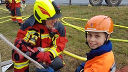 Felix und Johannes hocken in Feuerwehrausrüstung auf dem Boden.