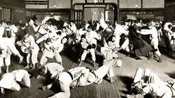 Schwarz-Weiß-Bild: Viele Judokämpfer in einer Halle.