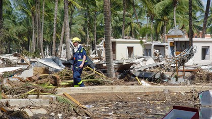 Ein Helfer des THW vor völlig zerstörten Gebäuden inmitten einer Palmenlandschaft.