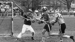 Historische Schwarzweißaufnahme einer Lacrosse-Spielszene mit drei Spielern vor dem Tor in Aktion.