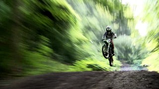 Motocrossfahrer auf Waldweg im Sprung.