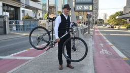Schick gekleideter Mountainbiker hebt in der Stadt sein Fahrrad hoch.