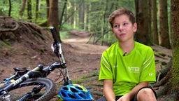 Konrad sitzt im Wald, sein Fahrrad liegt neben ihm.