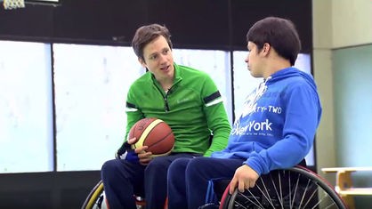 Johannes und Sven sitzen nebeneinander im Rollstuhl, Johannes hält einen Basketball.