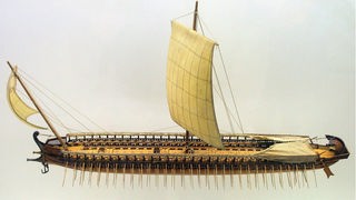 Modell eines rudergetriebenes Kriegsschiffs aus der Antike mit drei gestaffelt angeordneten Reihen von Riemen.