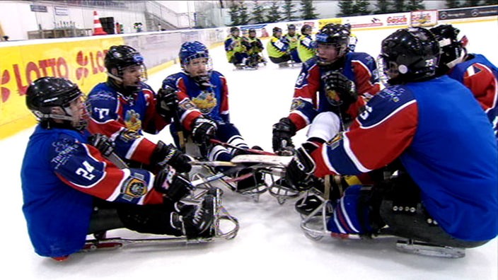 Sledgehockey-Team sitzt bei Besprechung auf dem Eis.