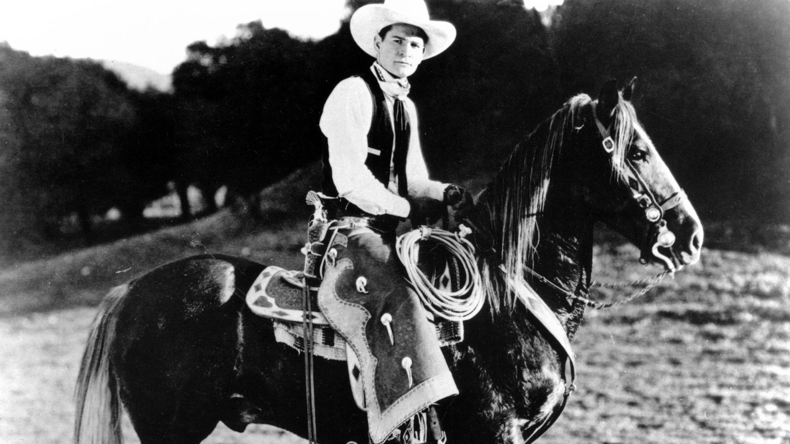 Schwarz-weiß Foto: Yakima Canutt in Western-Kleidung auf einem Pferd.