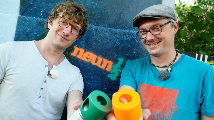 Robert und Sprayer Martin Scholz stehen mit Spraydosen in den Händen vor einer Graffiti-Wand