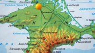 Stecknadel mit orangenem Kopf steckt auf einer Landkarte auf der Krim.