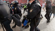 Russische Polizisten tragen Demonstranten.