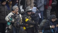 Soldat mit Kind auf dem Arm zwischen flüchtenden Menschen.