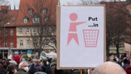 Plakat mit einem Piktogramm, auf dem ein Männchen Müll in einen Papierkorb wirft, mit der Aufschrift "Put ...in".