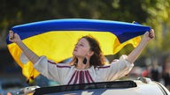Eine Frau schaut aus dem Schiebedach eines Autos und hält eine ukrainische Flagge. 