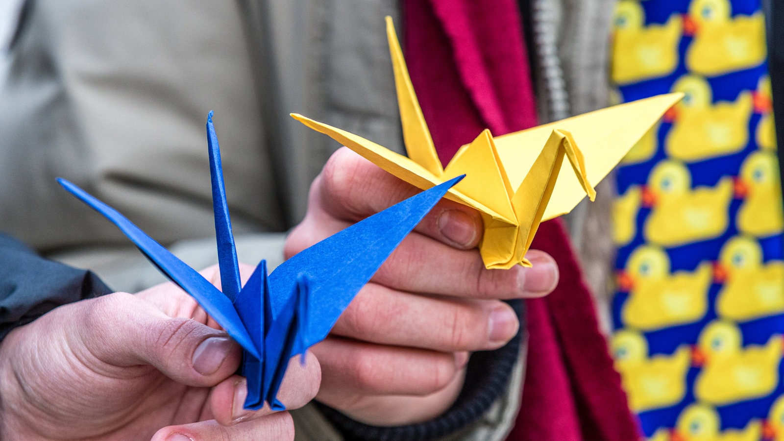 Zwei Jugendliche zeigen aus blauem und gelbem Papier gefaltete Kraniche.