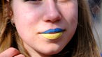 Eine junge Frau auf einer Demonstration in Brüssel mit blau-gelb geschminkten Lippen. 