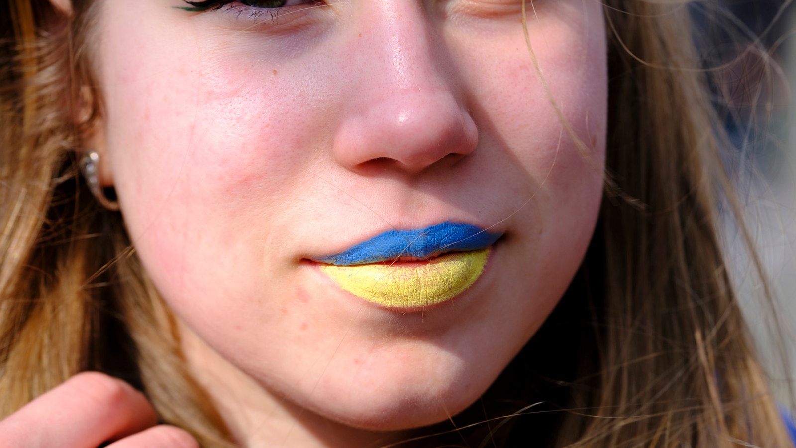 Eine junge Frau auf einer Demonstration in Brüssel mit blau-gelb geschminkten Lippen. 