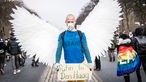 Ein Mann mit weißen Flügeln trägt auf einer Demonstration in Berlin ein Schild mit der Aufschrift "Putin to Den Haag".