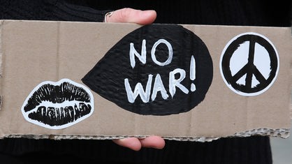 Hand hält Pappe mit Schrift 'No War', schwarzen Lippen und Friedenszeichen.
