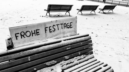 Verschneite Bänke, auf einer Bank steht "Frohe Festtage" in den Schnee geschrieben.