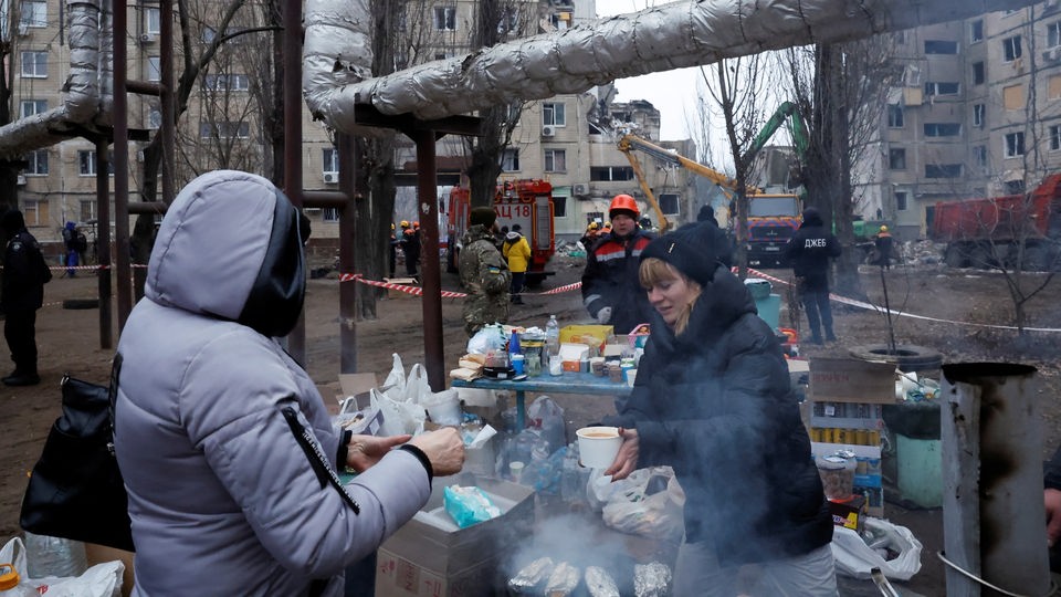 Eine Frau verteilt warmes Essen vor den Trümmern eines Wohnblocks in Dnipro.