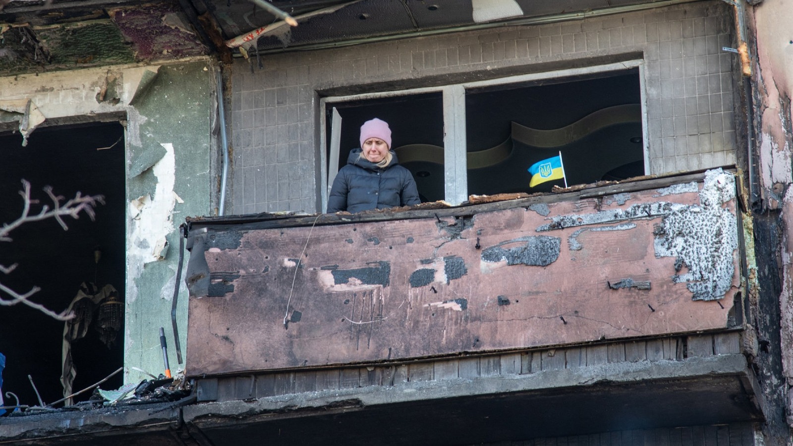 Eine Bewohnerin von Kiew steht mit einer kleinen ukrainischen Fahne auf dem Balkon ihres zerstörten Wohnhauses.