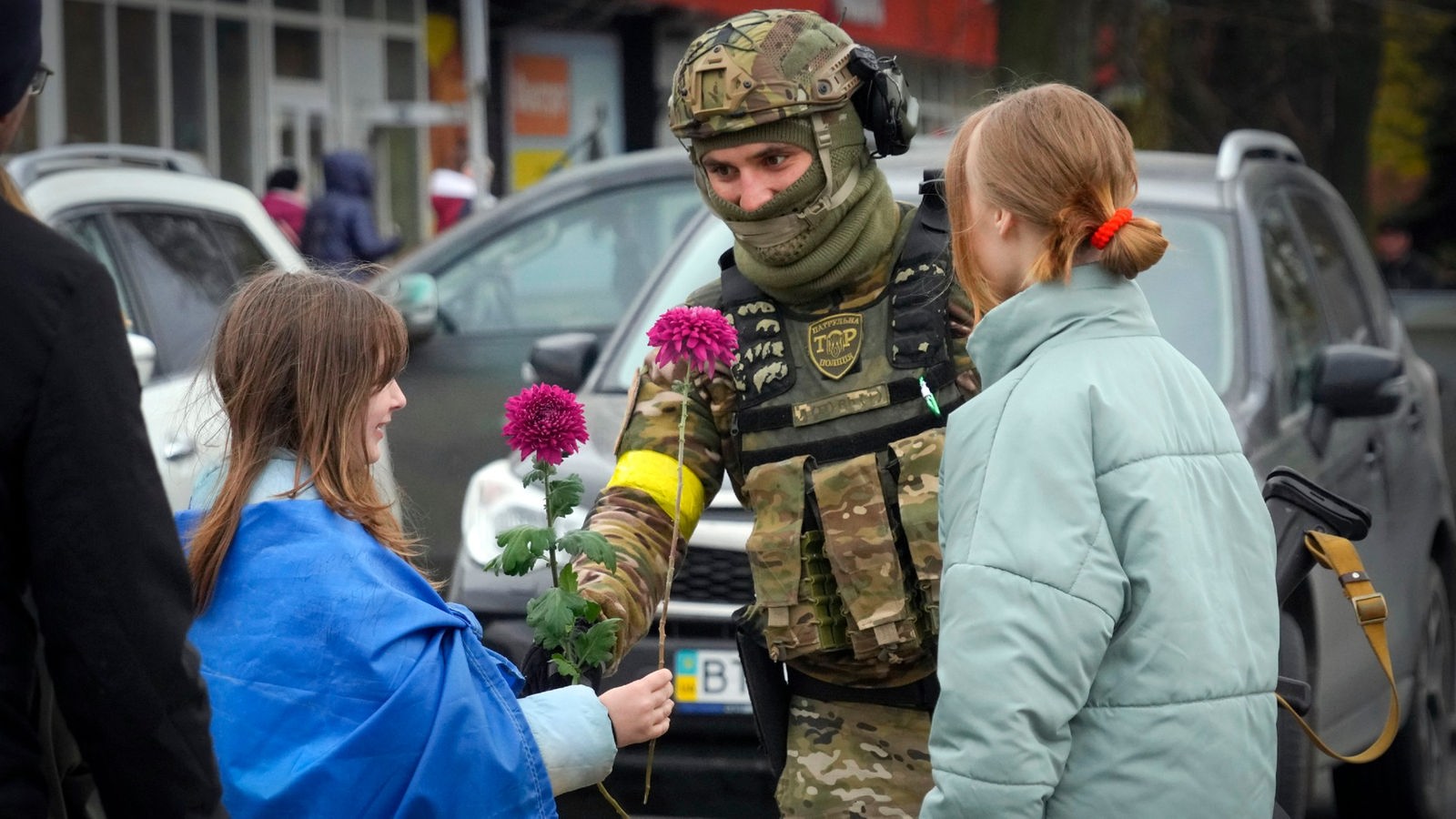 Ein Mädchen mit ukrainischer Fahne um die Schultern reicht einem ukrainischen Soldaten eine Blume.