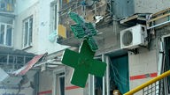 Ein beschädigtes grünes Kreuz hängt vor einer Apotheke.