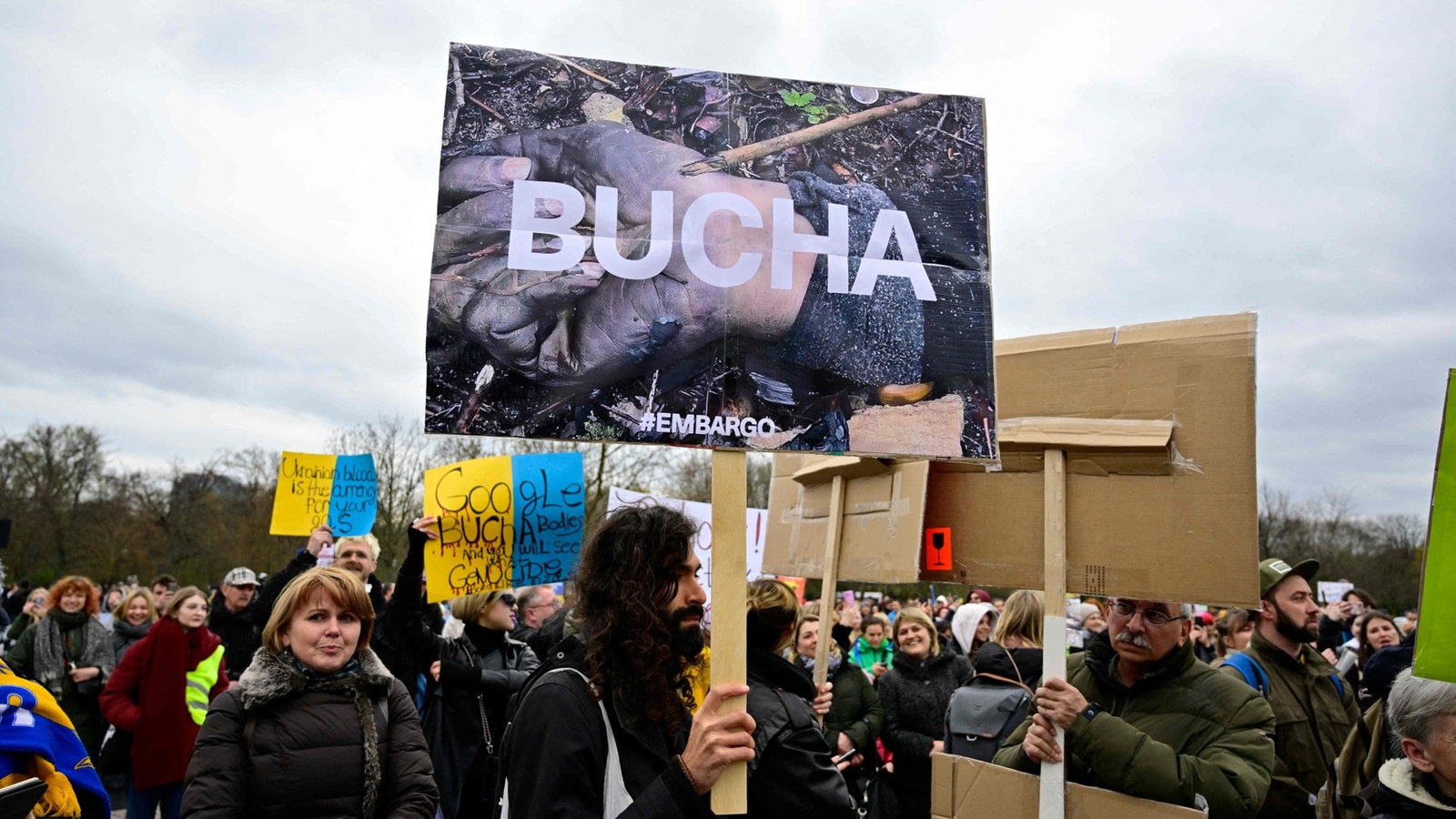 Demonstranten, einer hält ein Schild mit der Aufschrift 'Bucha, #embargo'.
