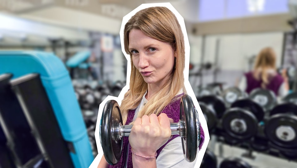 Jana hält eine Hantel in der Hand. Im Hintergrund sieht man ein Fitnessstudio.