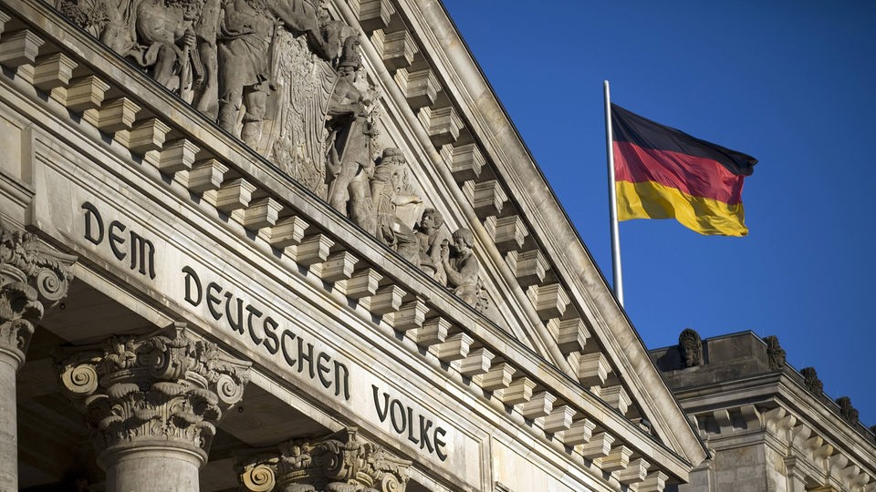 Deutschlandfahne weht hinter Ausschnitt von Reichstag.
