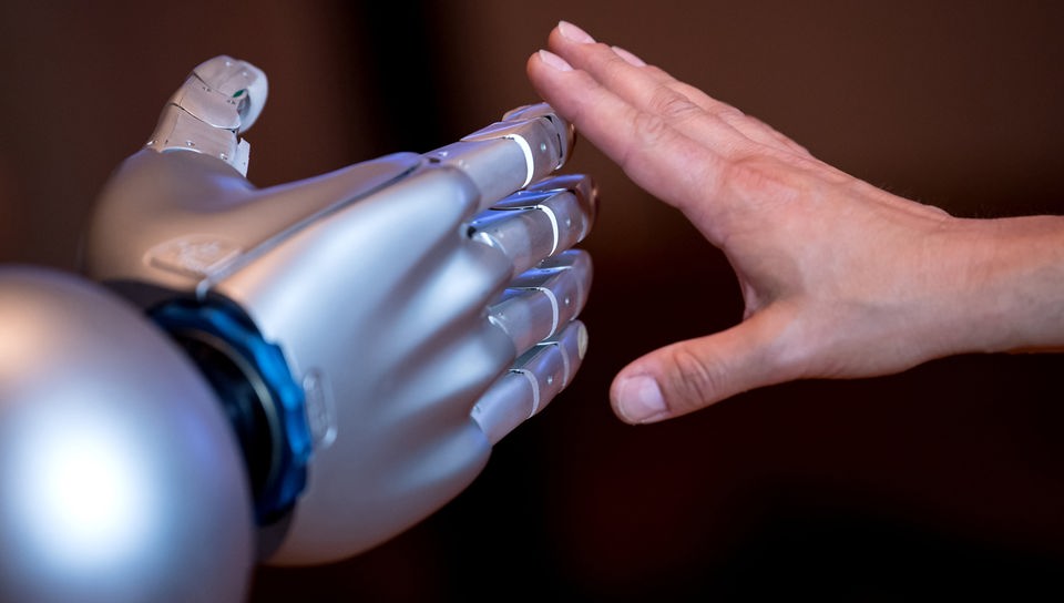 Eine menschliche Hand streckt sich einer Roboterhand entgegen.