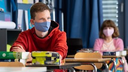 Schüler sitzt mit Maske in Klassenraum.