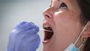 Hand mit Gummihandschuh steckt Wattestäbchen in den geöffneten Mund einer Frau.